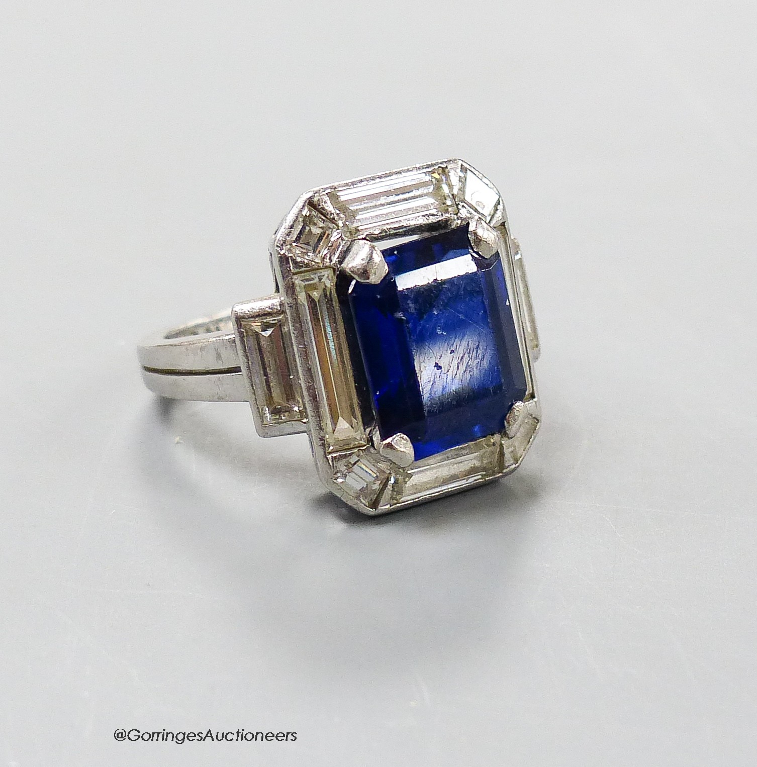 A white metal (stamped plat? synthetic sapphire, baguette and trapeze cut diamond set dress ring, size L, gross weight 11.1 grams